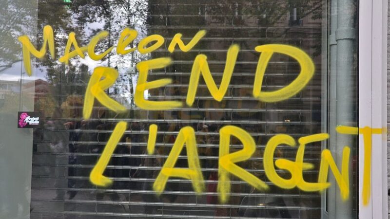 Yellow protest graffiti on a Paris shopfront reading Macron rend l argent